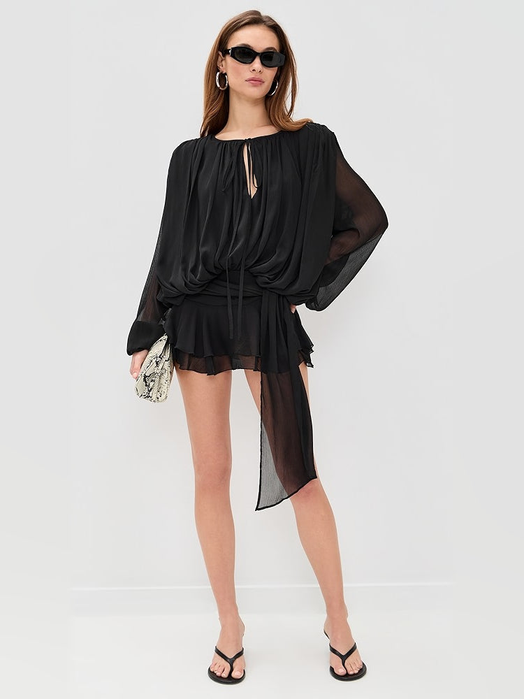 Black mini dress with draped bodice, long sheer sleeves, and tiered ruffle hem