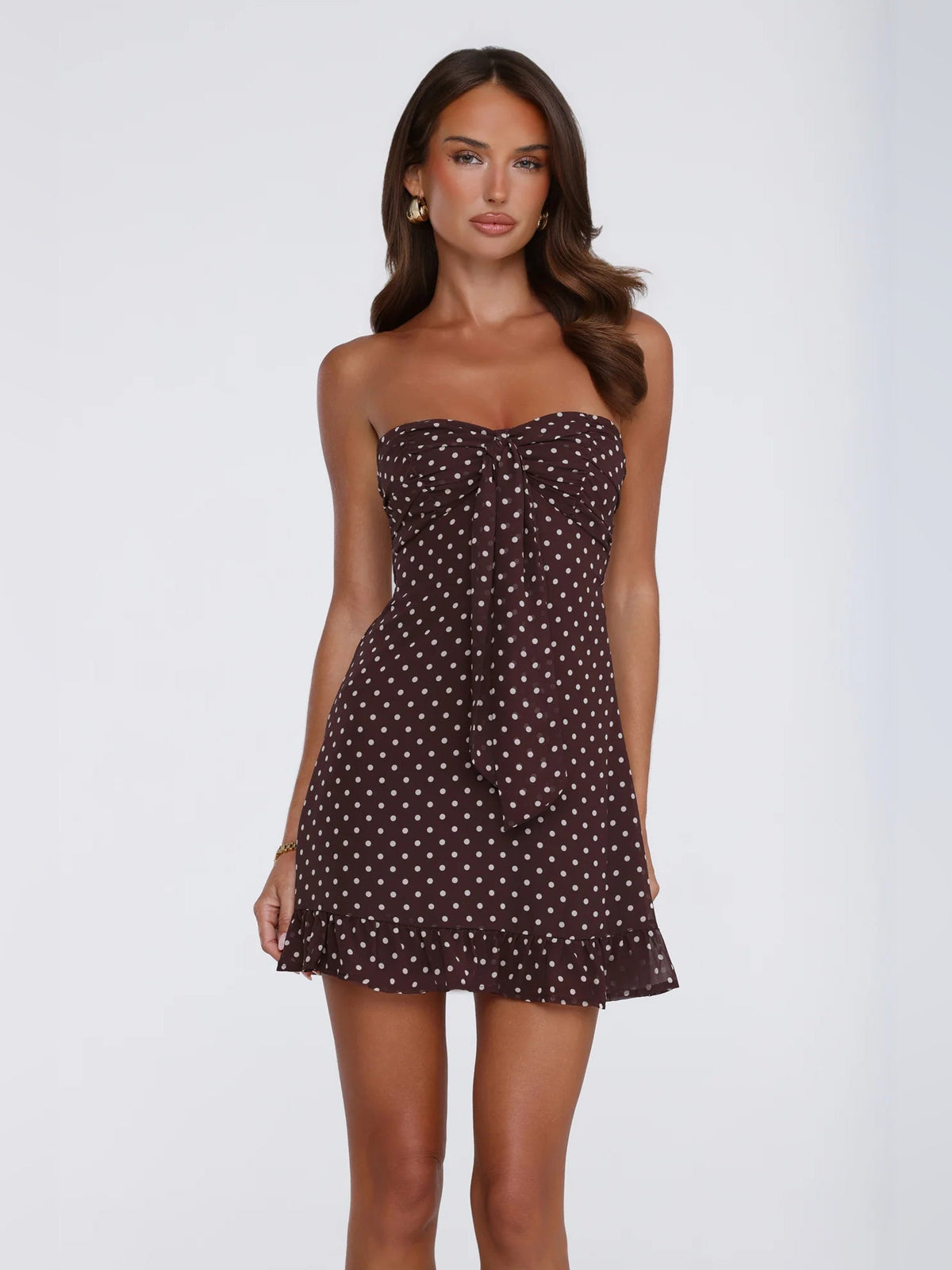 Brown strapless mini dress with white polka dots, gathered bust and ruffled hem.