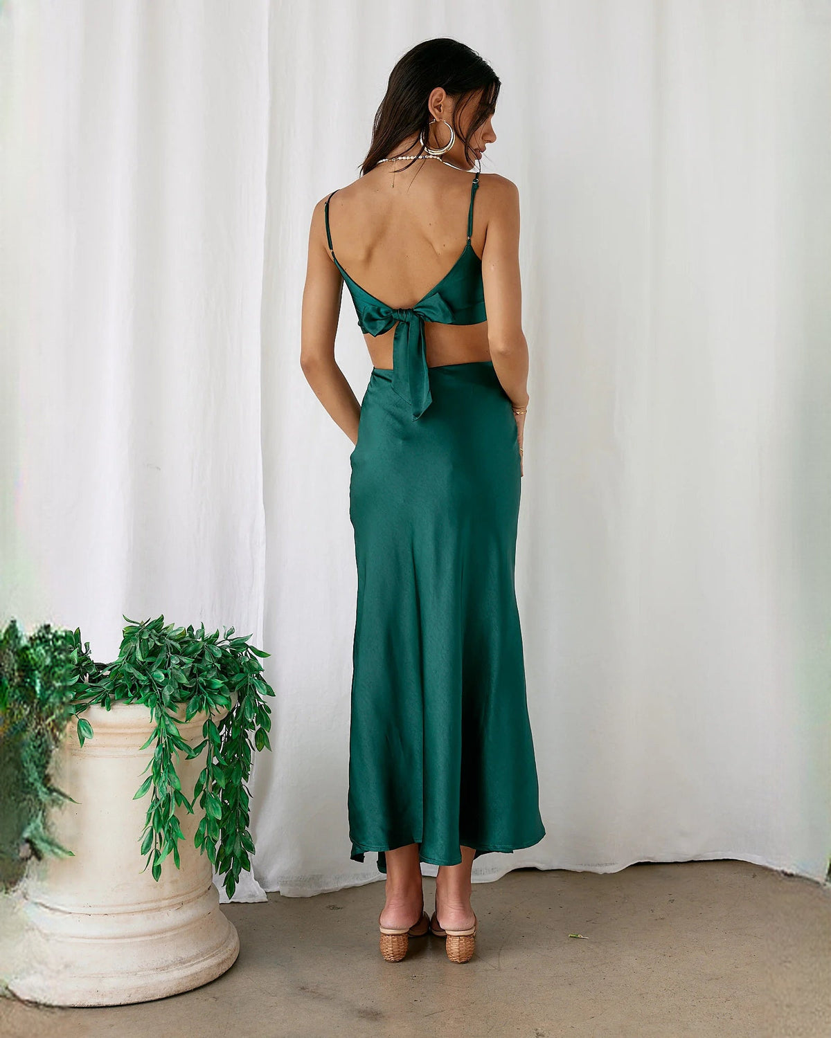 Back view of emerald green satin sleeveless maxi dress with crisscross back straps and open back.