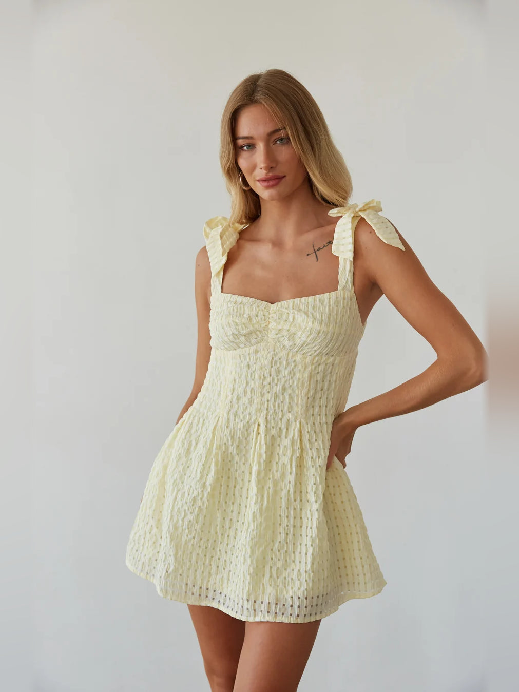 Cream mini dress with thin straps, square neckline, and ruffled bow accents