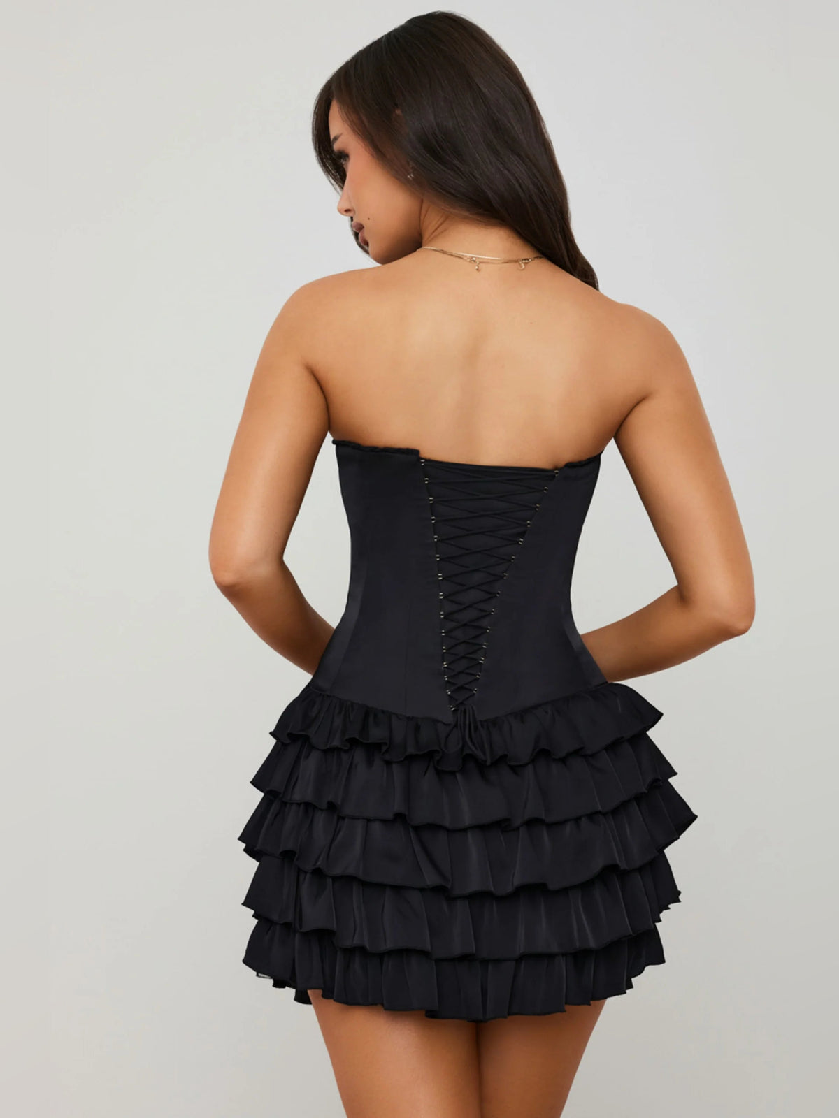 Black corset mini dress viewed from back, with tiered ruffle skirt and lace-up seams.