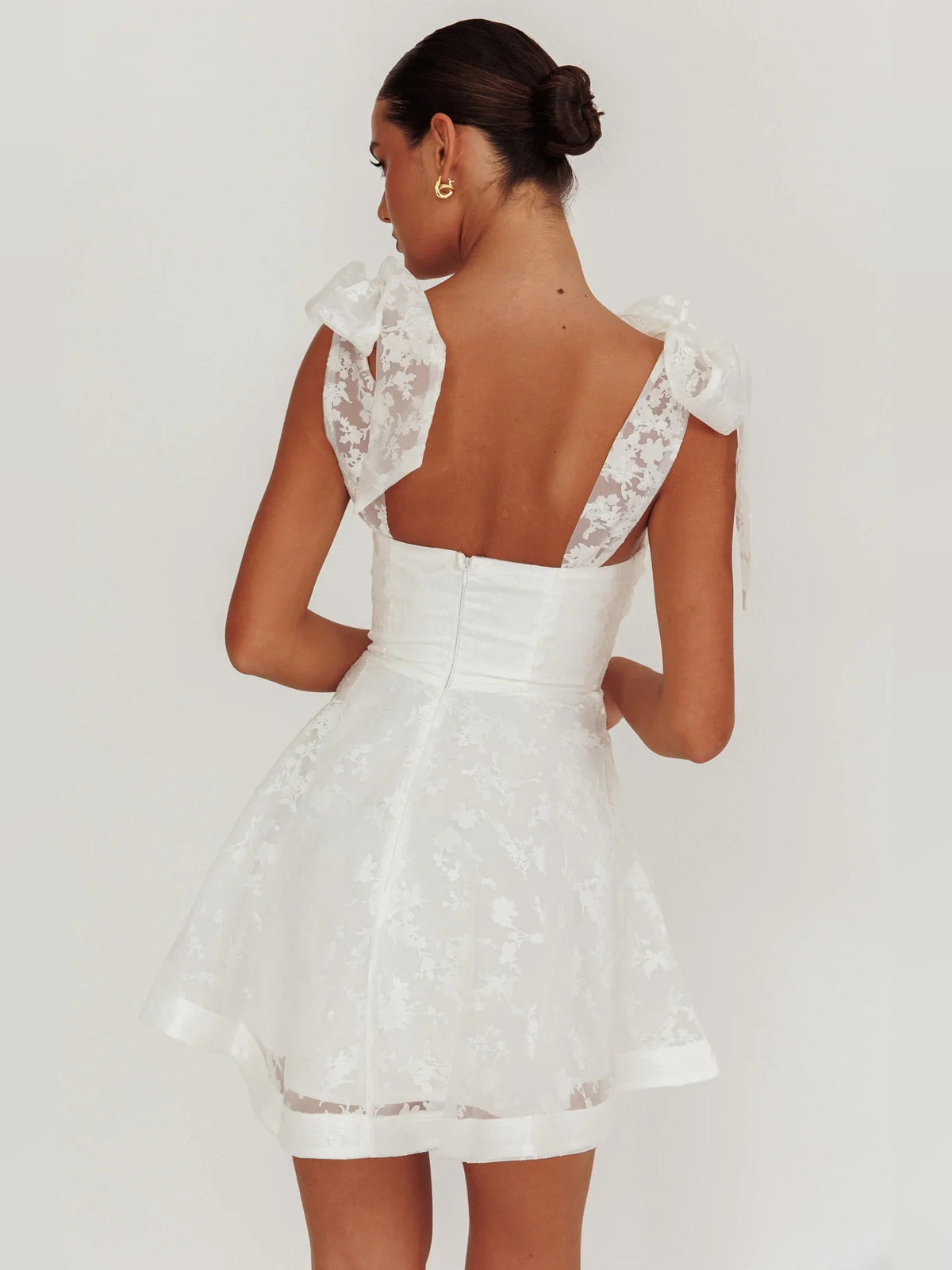 Ivory mini dress with open back, bow shoulder details, and layered organza floral skirt