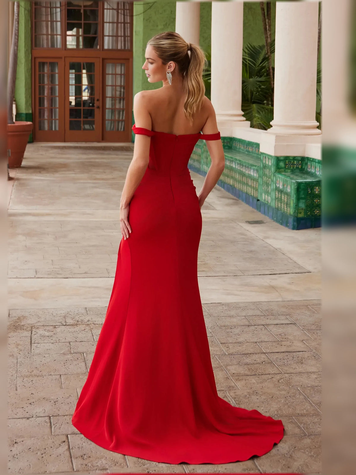 Red off-shoulder corset formal gown with open back and floor-length skirt, slit.