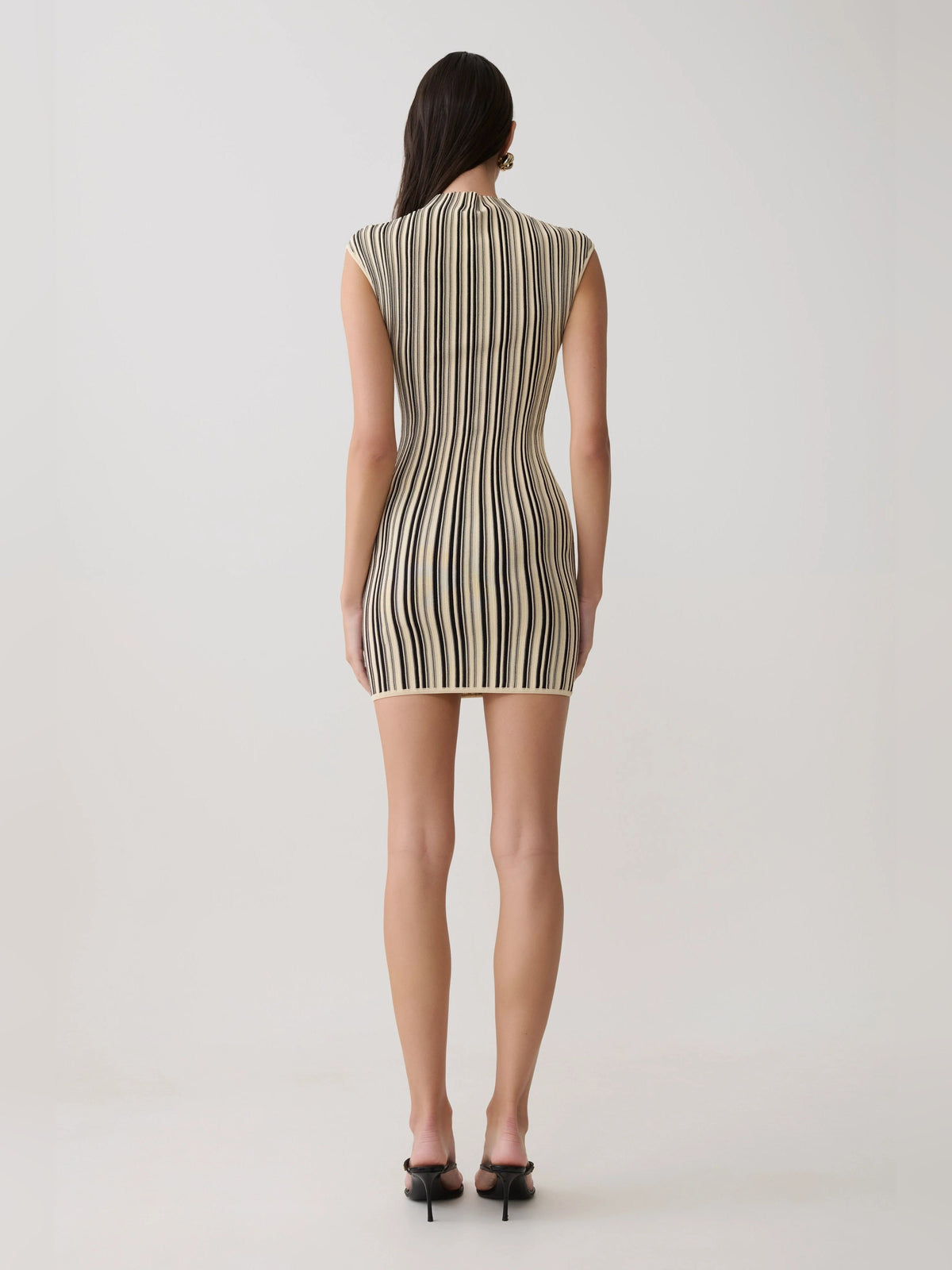 Back view of ivory sleeveless mini dress with vertical black and gold stripes, high neck