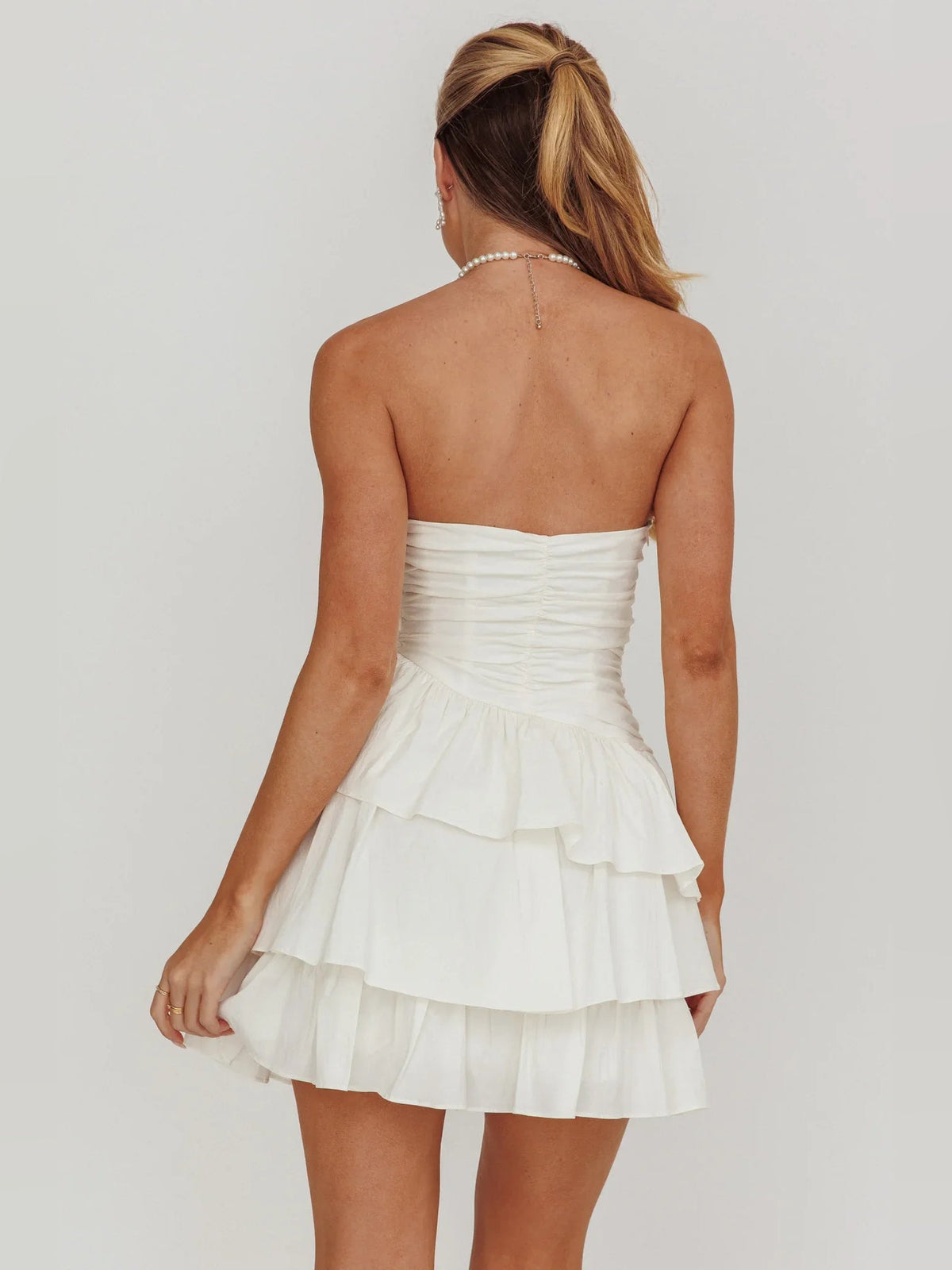 Back view of ivory strapless mini dress with ruched bodice and tiered ruffles