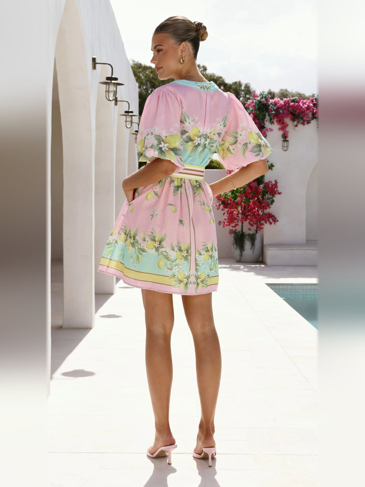 Pink floral mini dress with turquoise V-neck trim, short puff sleeves, gold ring waist belt.