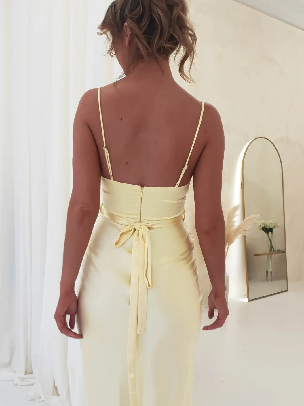 Back view of yellow satin mermaid dress with thin straps and fitted ruched waist bow