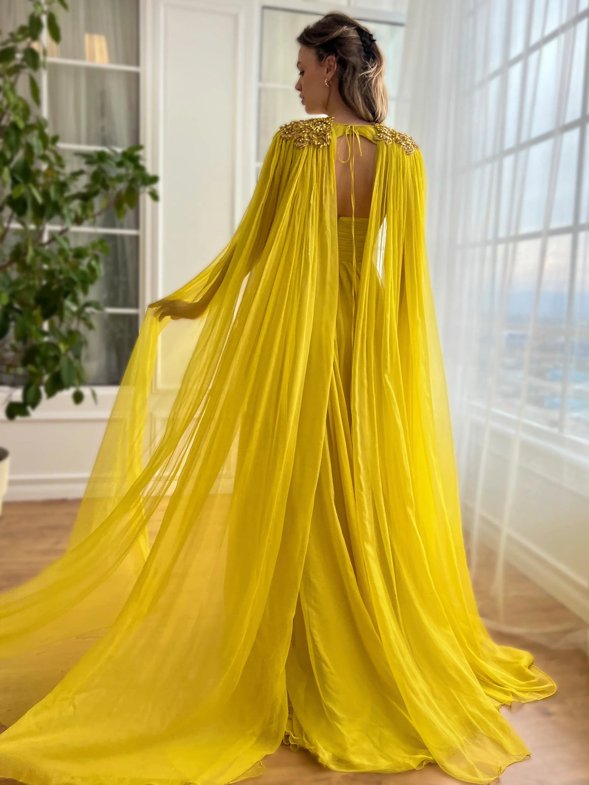 Yellow floor-length formal dress with front slit and flowing tulle cape, back view