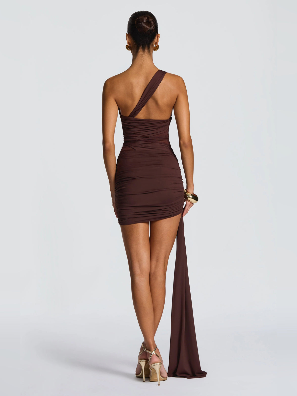 Brown one-shoulder ruched bodycon mini dress with crossback straps and long trailing drape.
