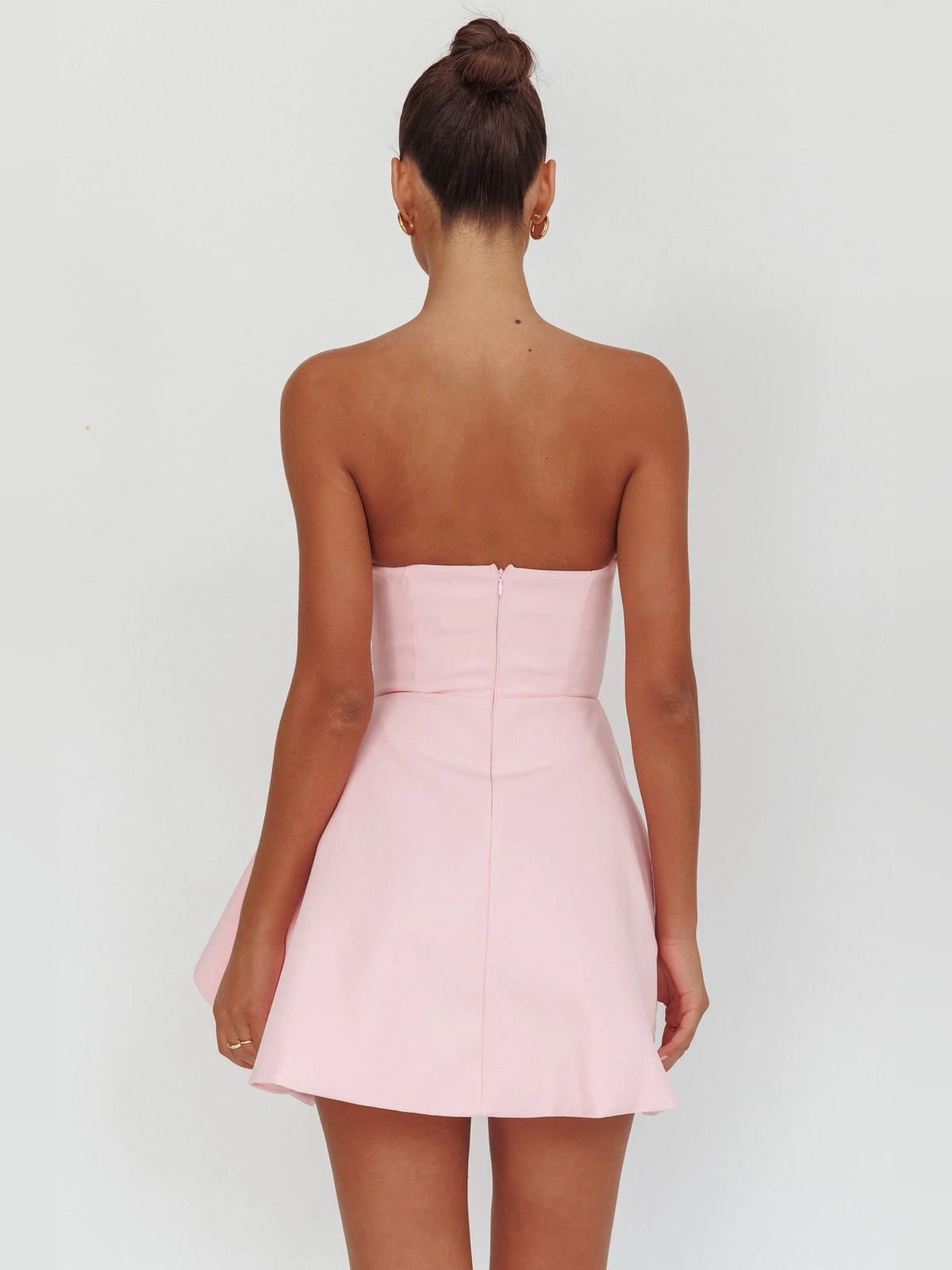 Pink strapless mini dress from back, ruched seams and flared layered hem