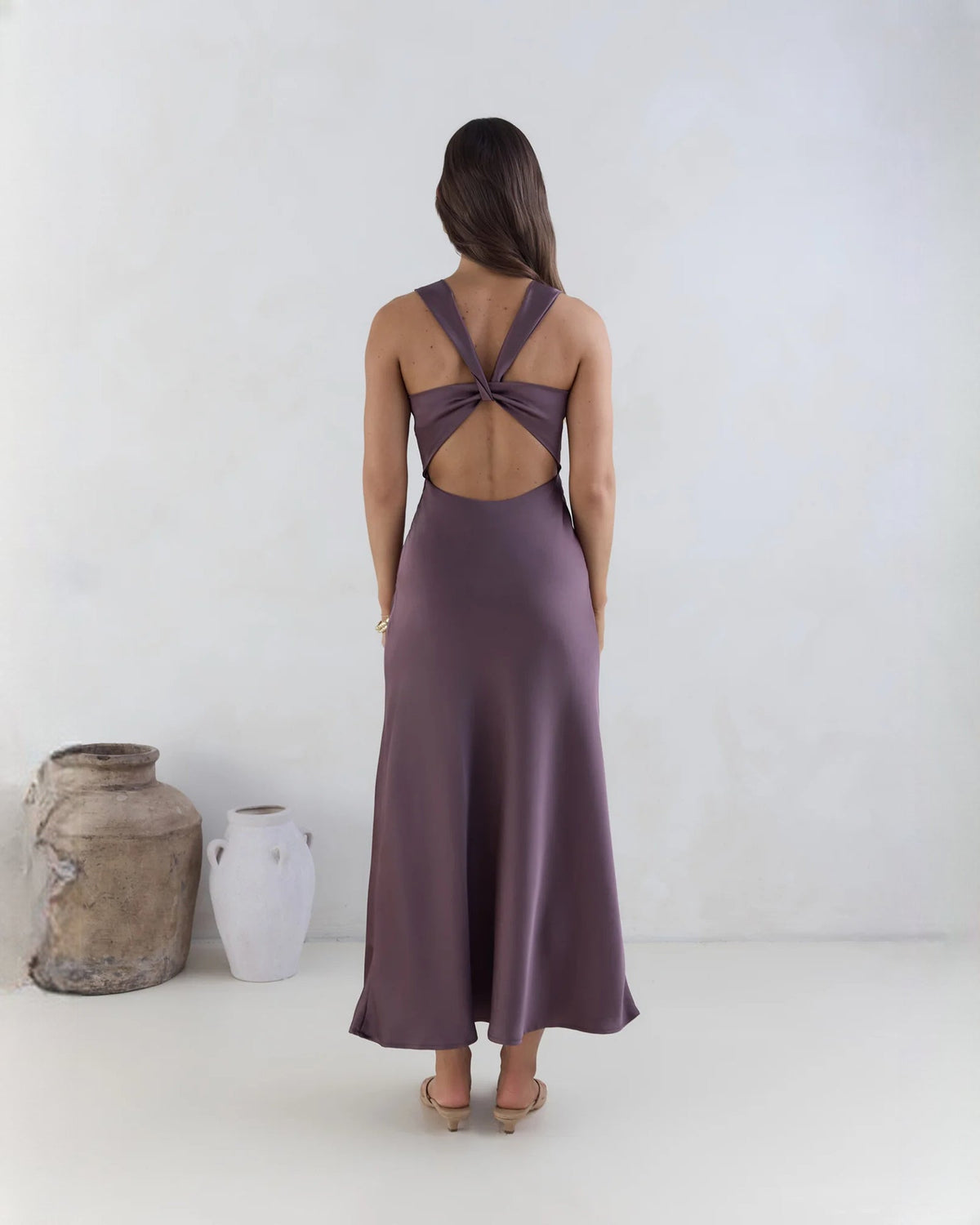 Purple satin sleeveless maxi dress with open back and crisscross knot detail.