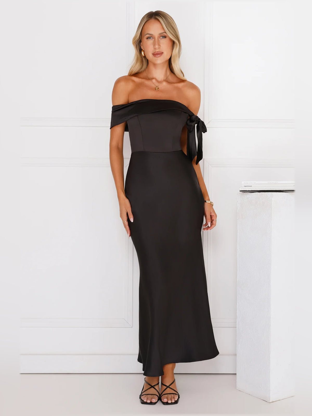 Black off-shoulder satin midi dress with ribbon bow at shoulder and sleek column fit