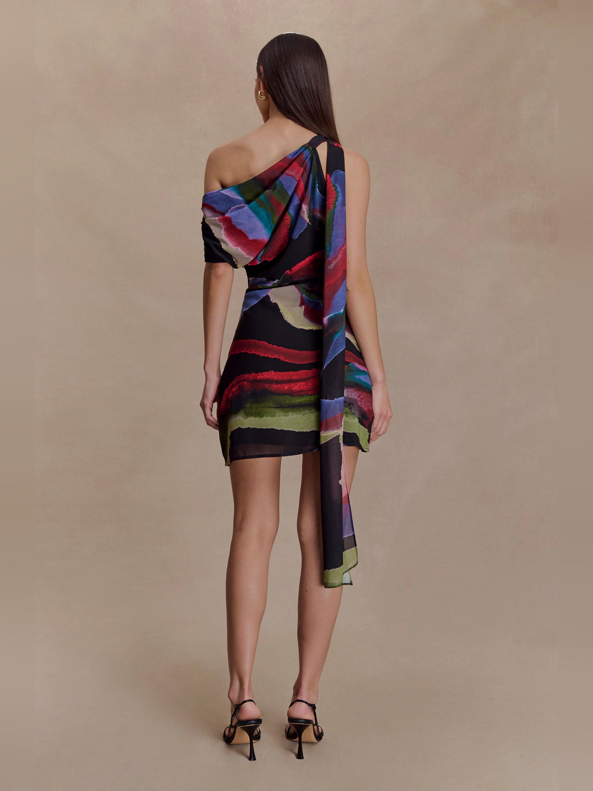 Back view: black mini dress with multicolor abstract print and draped one-shoulder panel.