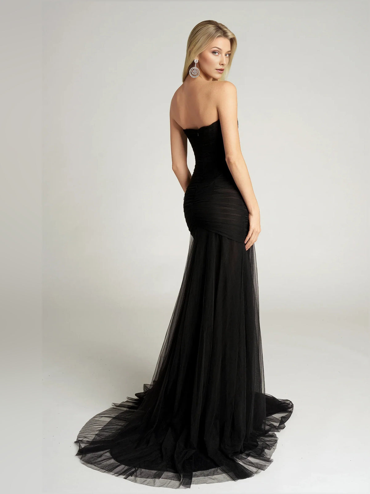 Black strapless sweetheart mermaid formal dress, side view with flowing tulle skirt.