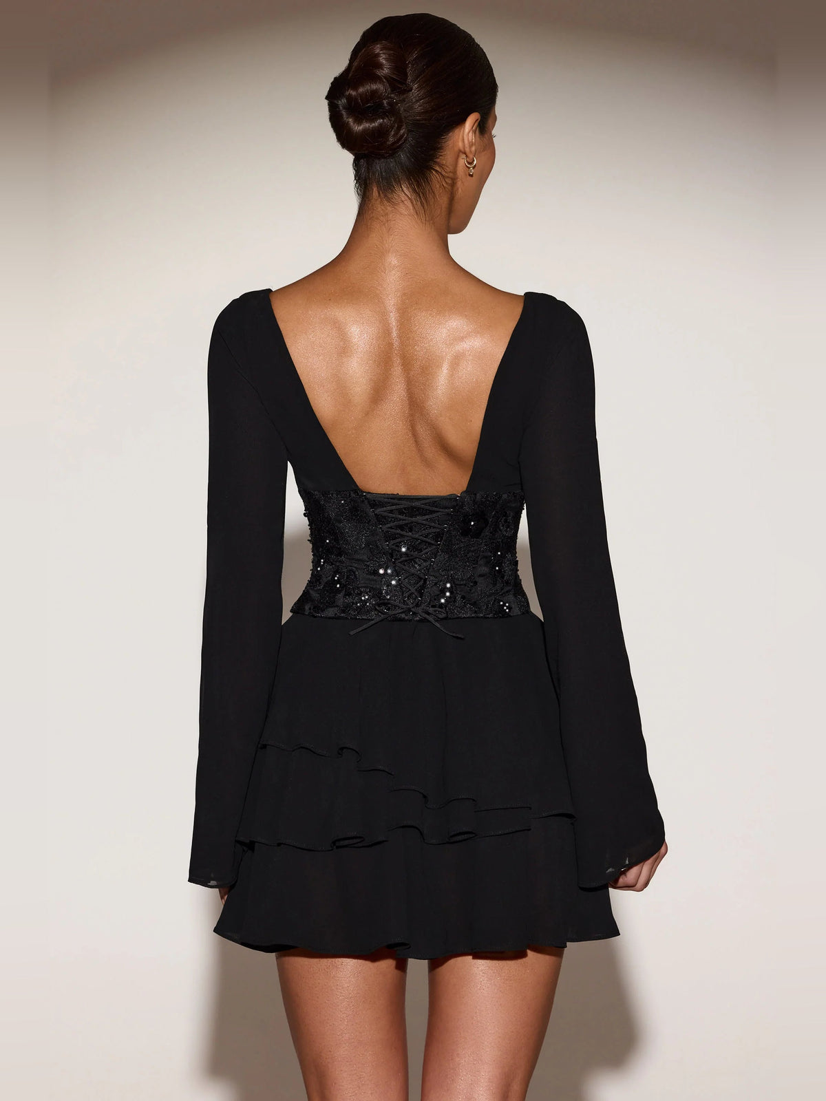 Black corset A-line mini dress, back view, long sleeves, V-back neckline, tiered skirt