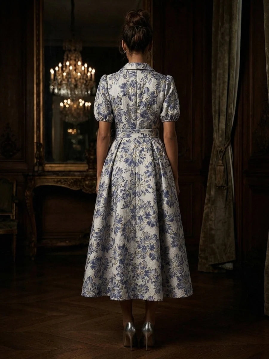 Back view of steel blue floral A-line tea-length dress with puff sleeves and pleated skirt