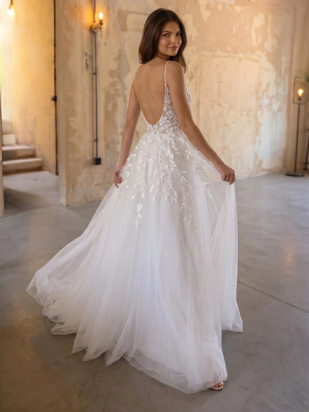 Ivory A-line tulle wedding dress showing low back with thin straps and floral lace bodice.