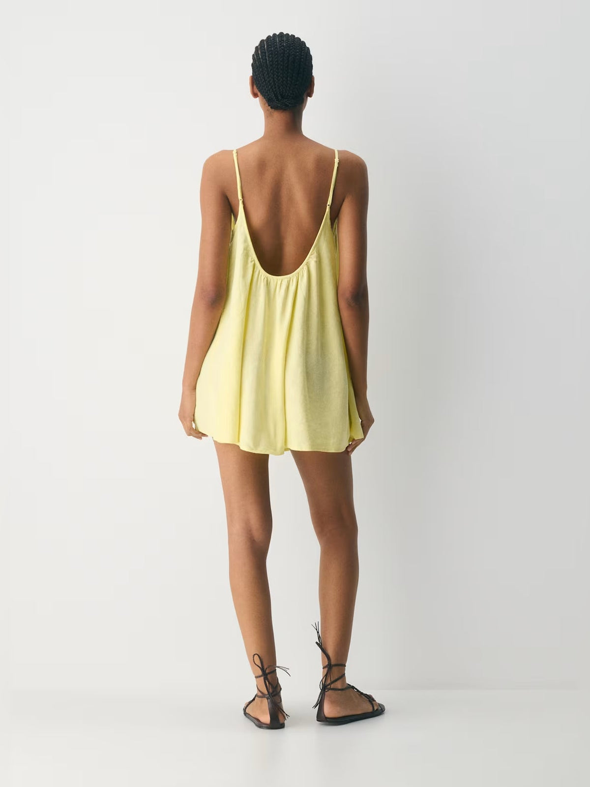 Back view of light yellow mini dress with thin straps and open-back scoop shape