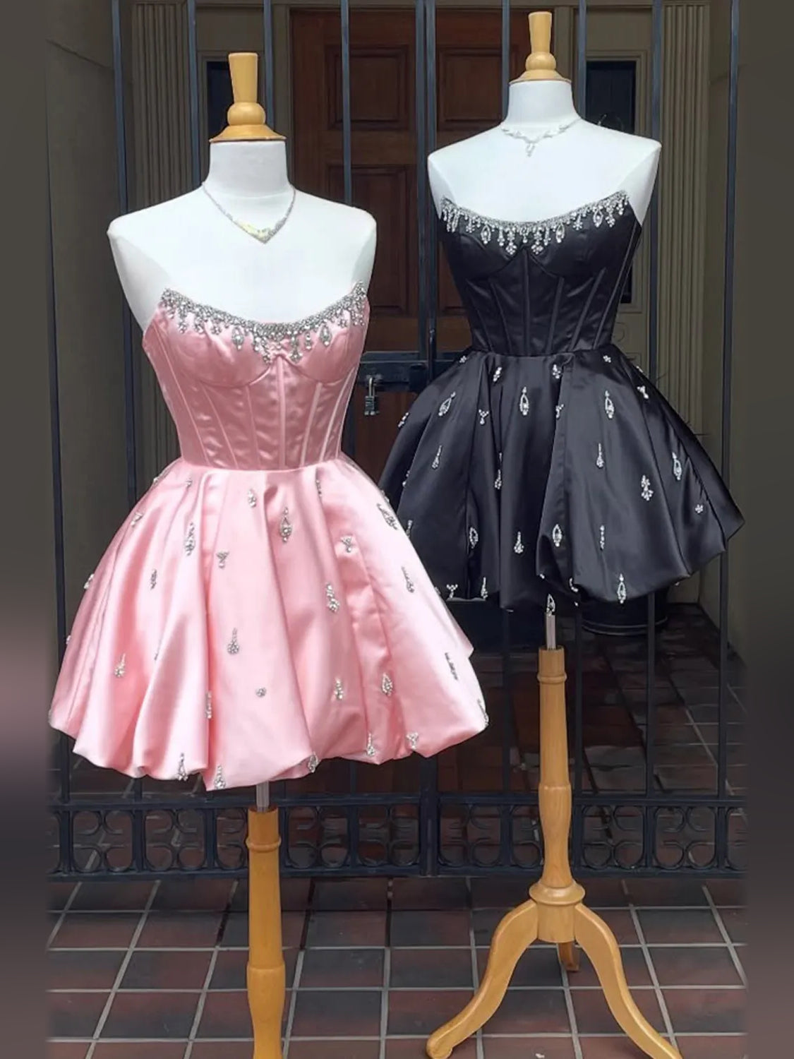 Pink and black satin mini dresses on mannequins, crystal-trim sweetheart corset bodices