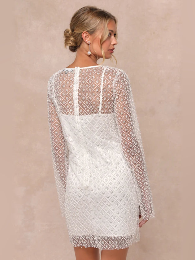 White sequin mini dress with open back detail and long sheer sleeves.