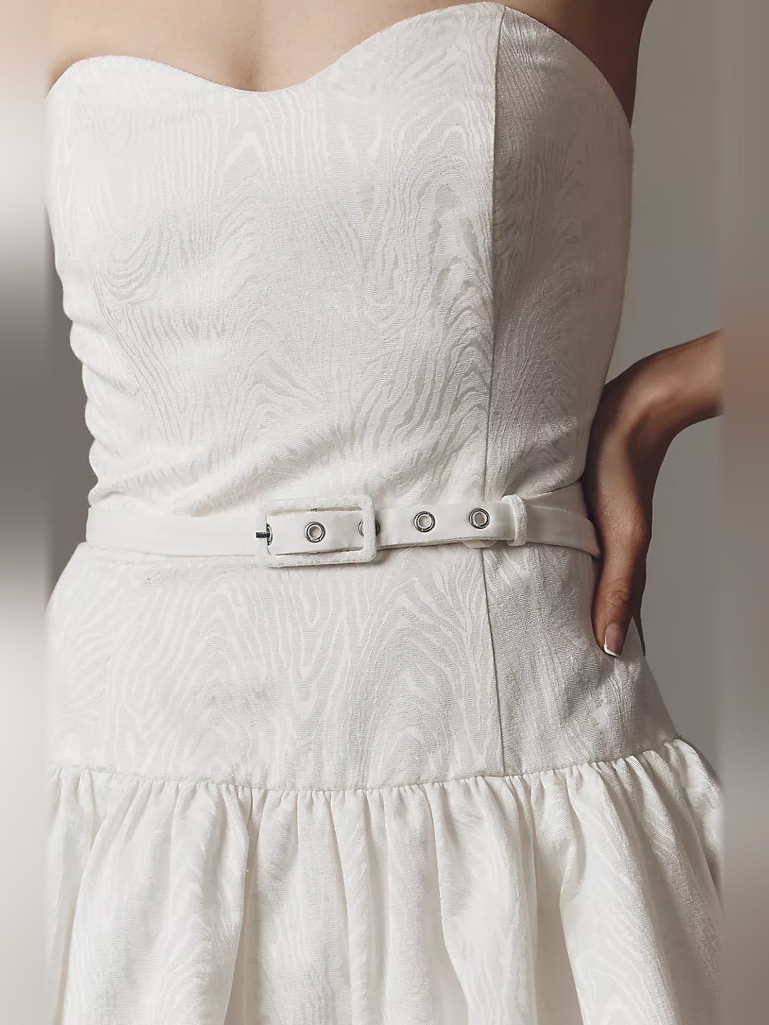 Close-up of white strapless dress with textured fabric and belt with metal grommets