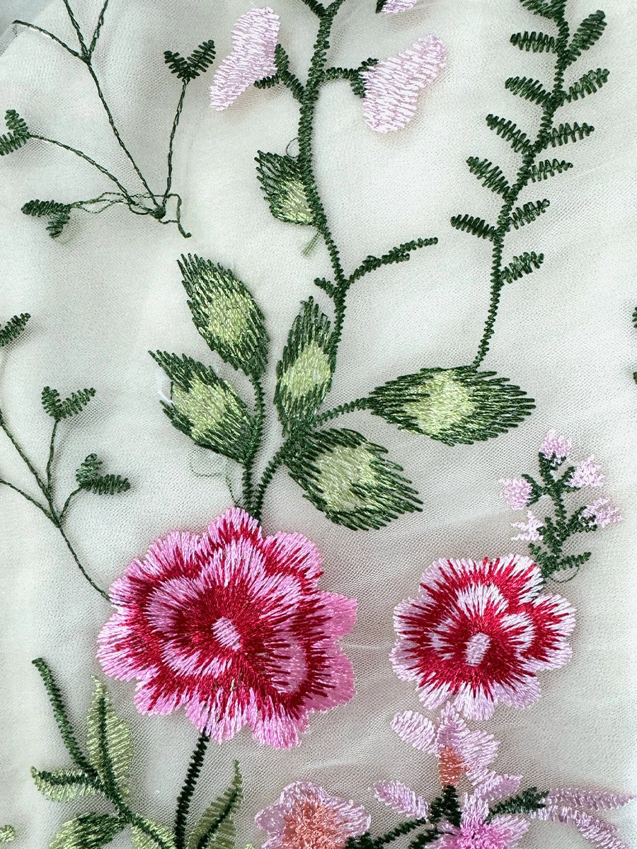 Close-up of embroidered floral motifs on sheer tulle fabric, pink and green