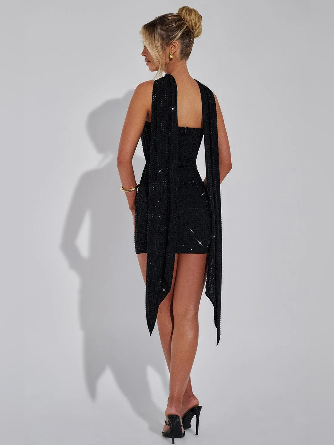 Black backless mini dress with sparkly fabric and flowing draped back panels