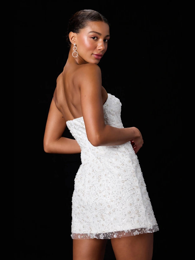 White strapless sequin mini dress in side pose, fitted waist and flared skirt hem