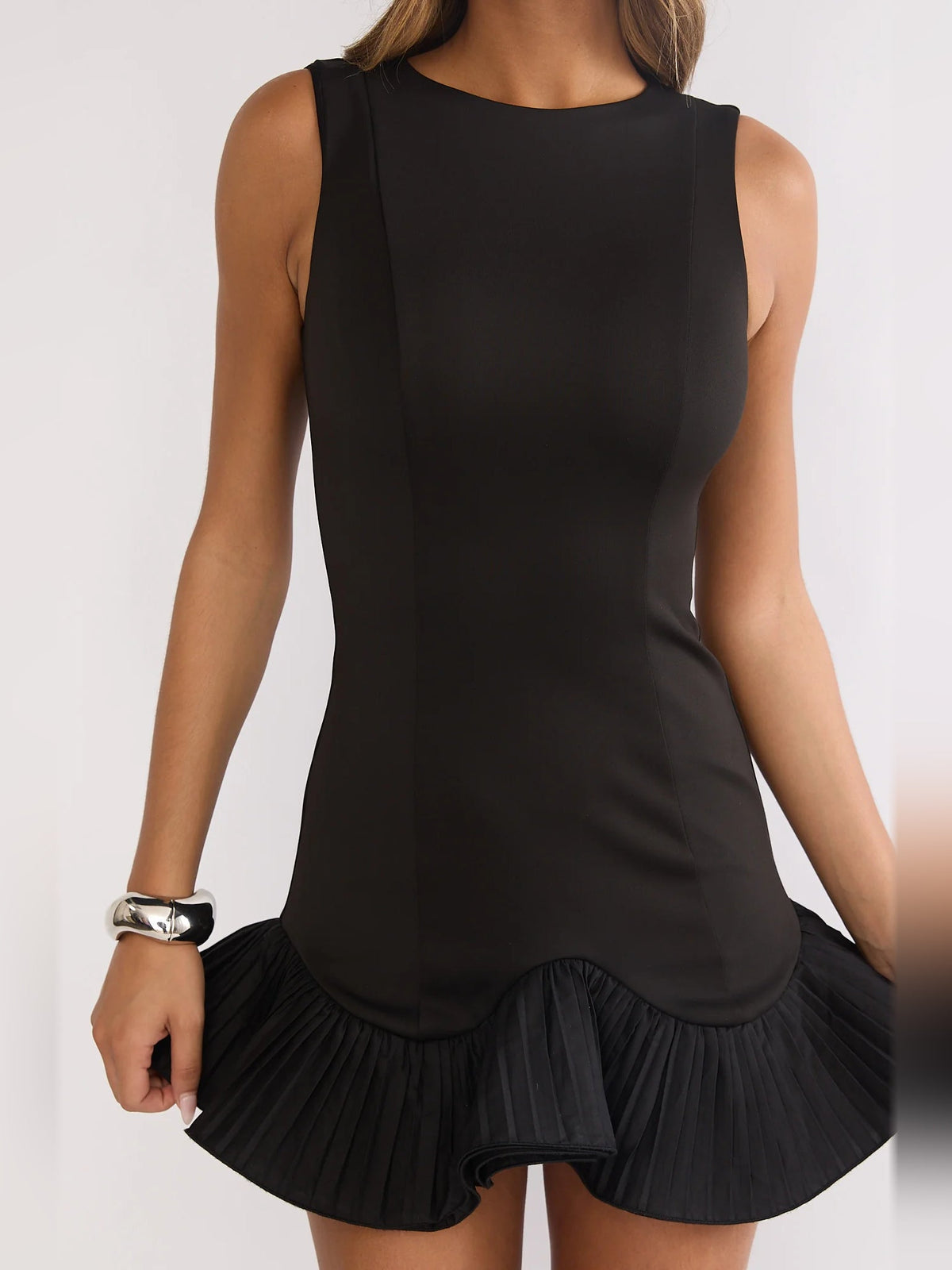 Black sleeveless mini dress with round neckline and pleated ruffle hem detail.