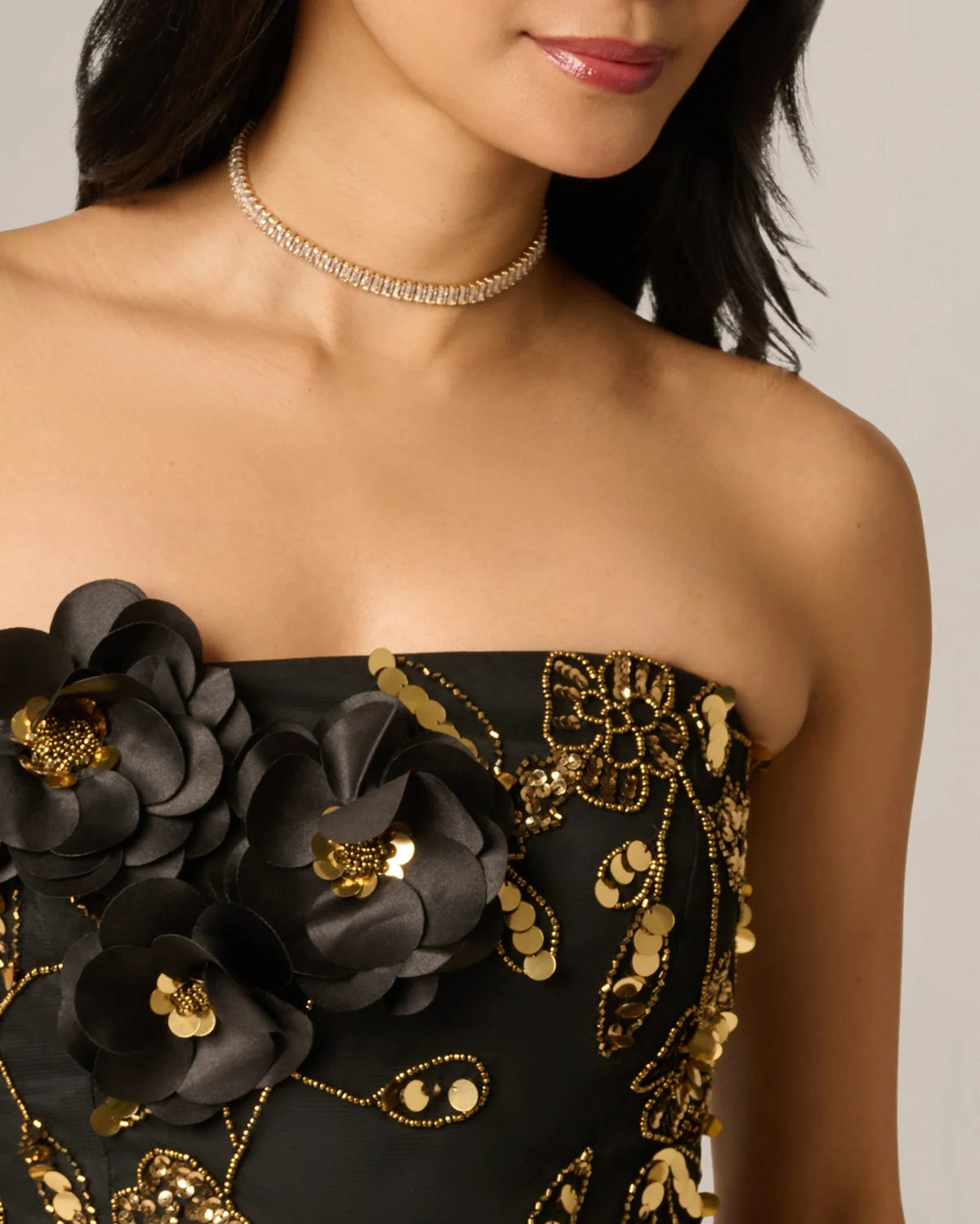 Strapless bodice close-up with black fabric, gold floral sequins and 3D applique flowers