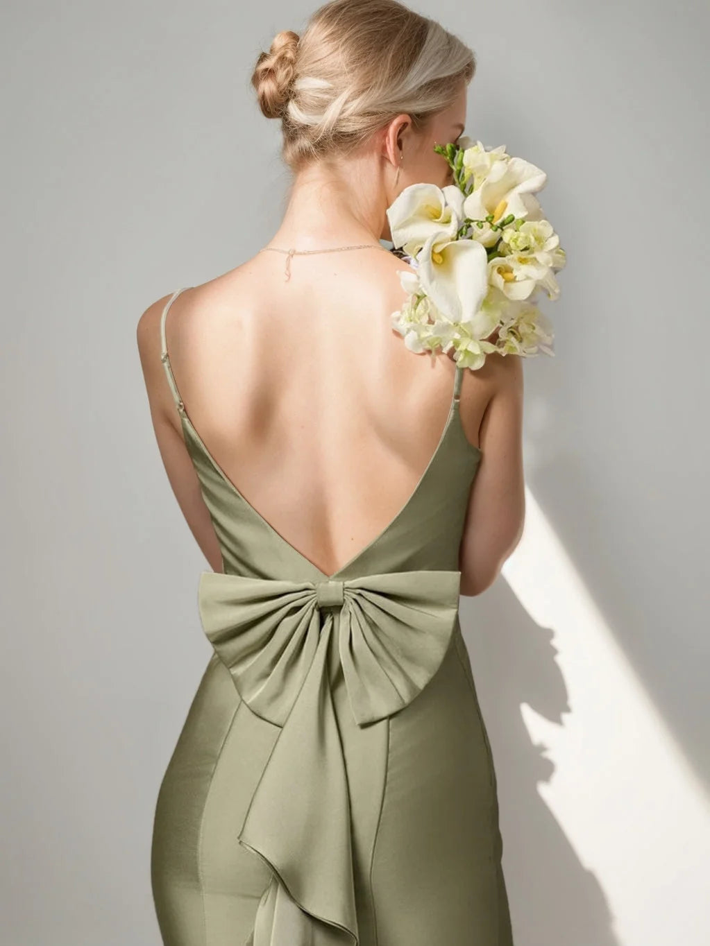 Back view of dusty sage satin dress with open V neckline and waist bow.