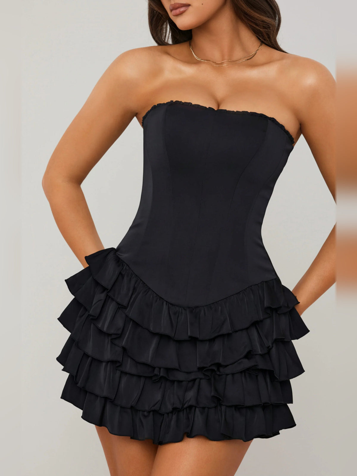 Front view of black strapless corset mini dress with tiered ruffle skirt and scalloped edges.