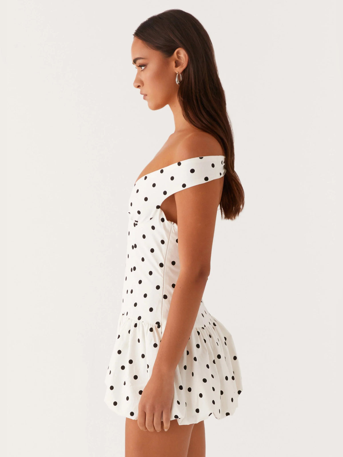 Off-shoulder mini dress side view in white with black polka dots, gathered waist, flared skirt