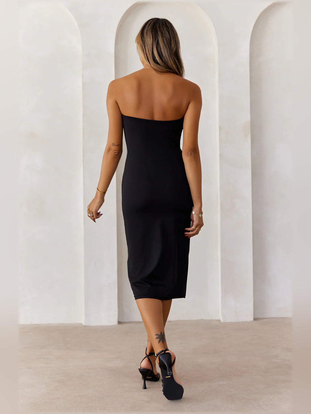 Black strapless bodycon midi dress from back view with exposed bare shoulders.