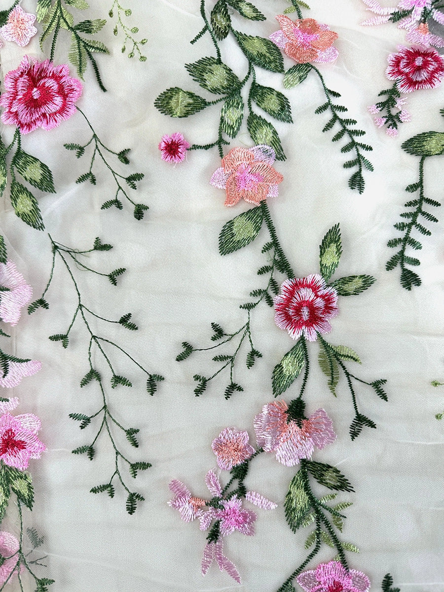 Close-up of multicolor floral embroidery with green leaves on white tulle