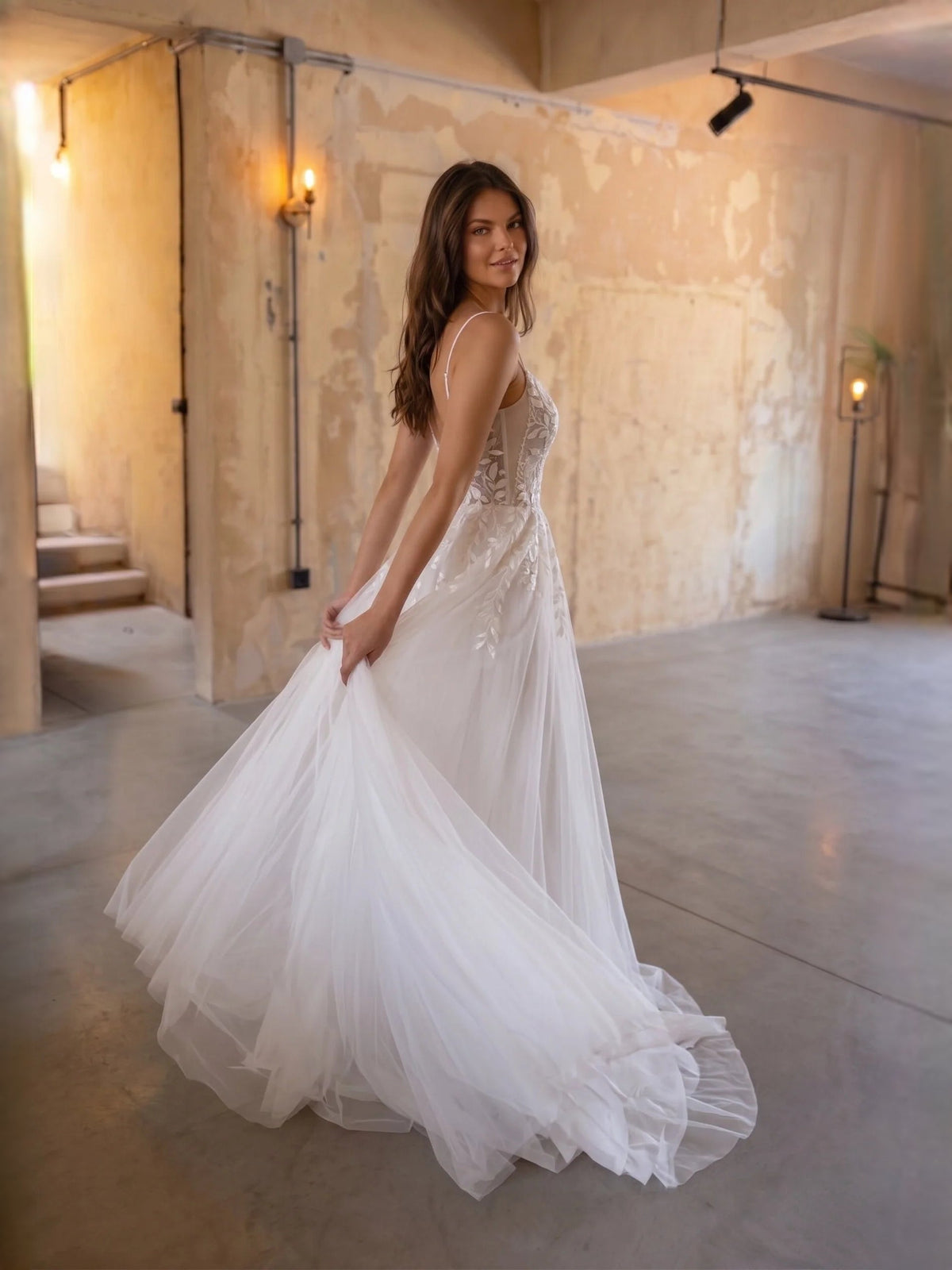 Ivory floral lace A-line tulle wedding dress in side view with thin straps and layered skirt.