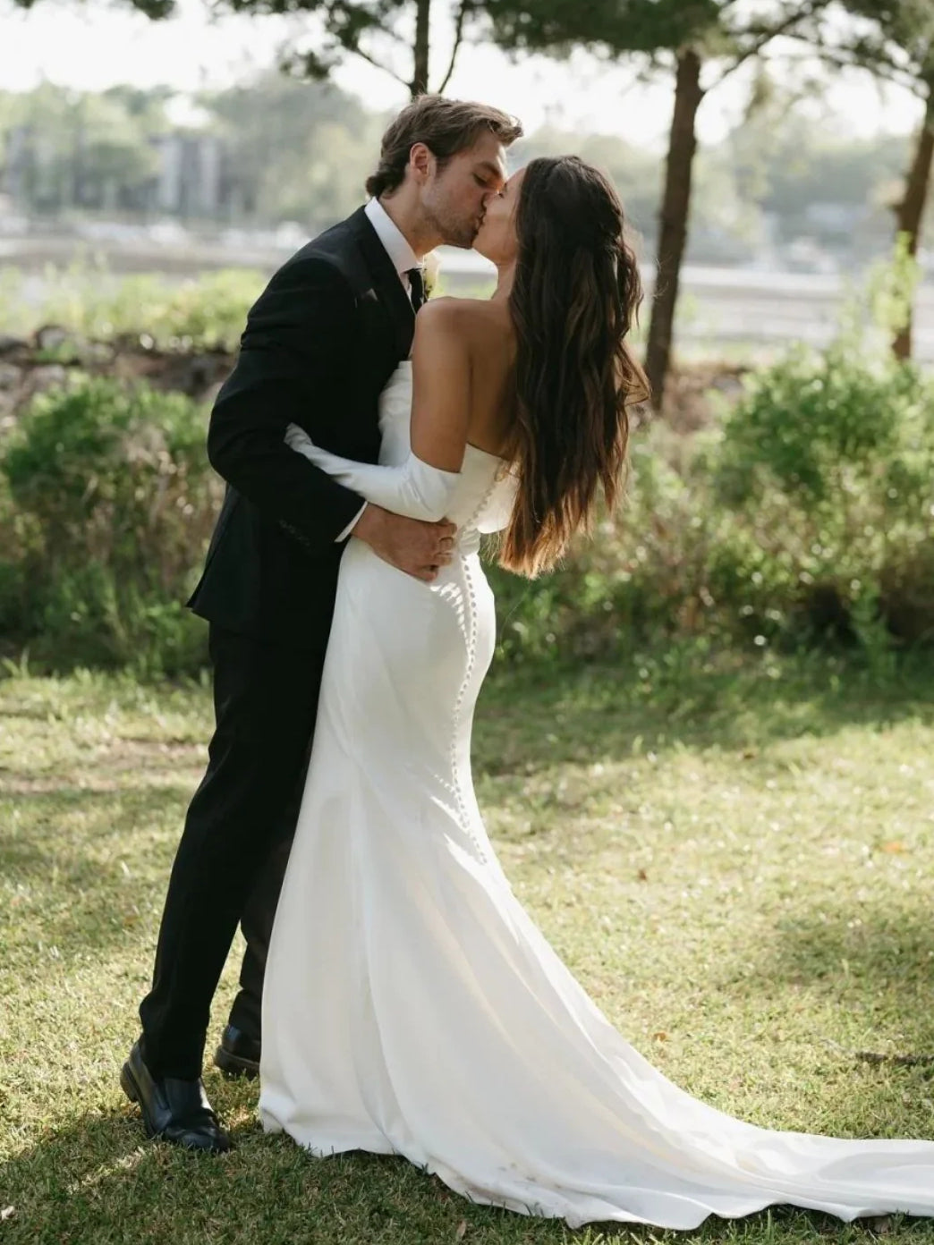 White mermaid wedding dress with long train, strapless fitted waist; bride in embrace