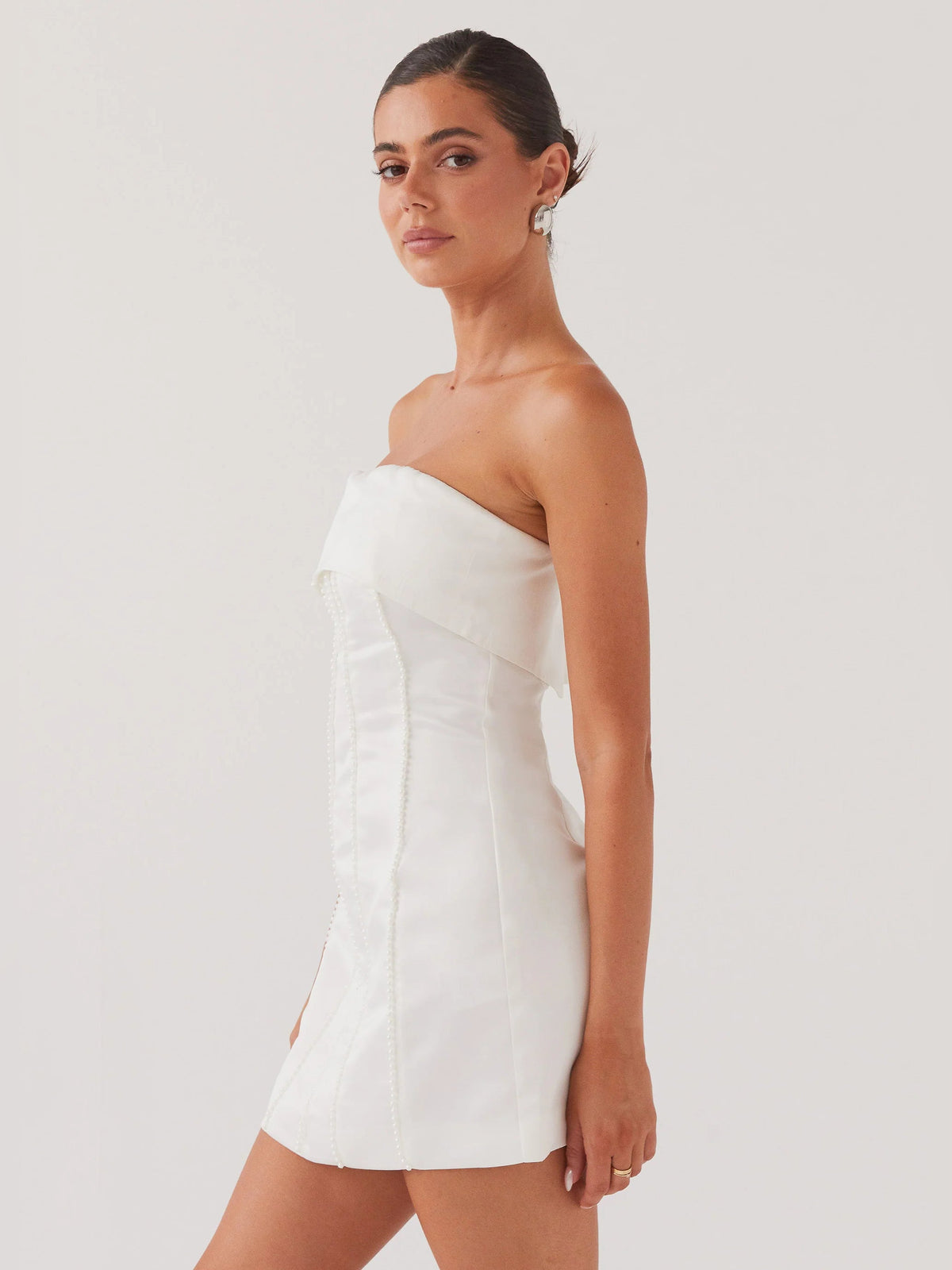 Pearl strapless mini dress in profile view with fitted seams and side slit detail