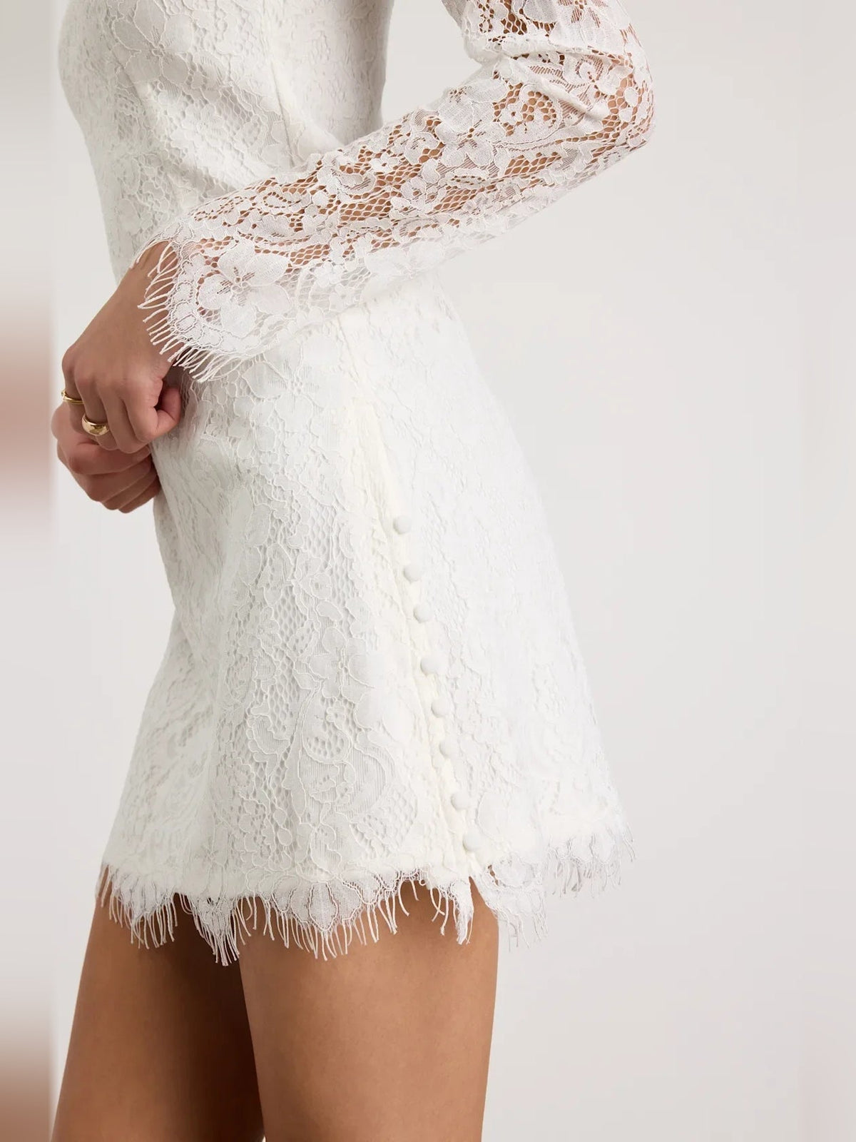 White lace long-sleeve mini dress close-up: floral sleeves and fringe trim hem
