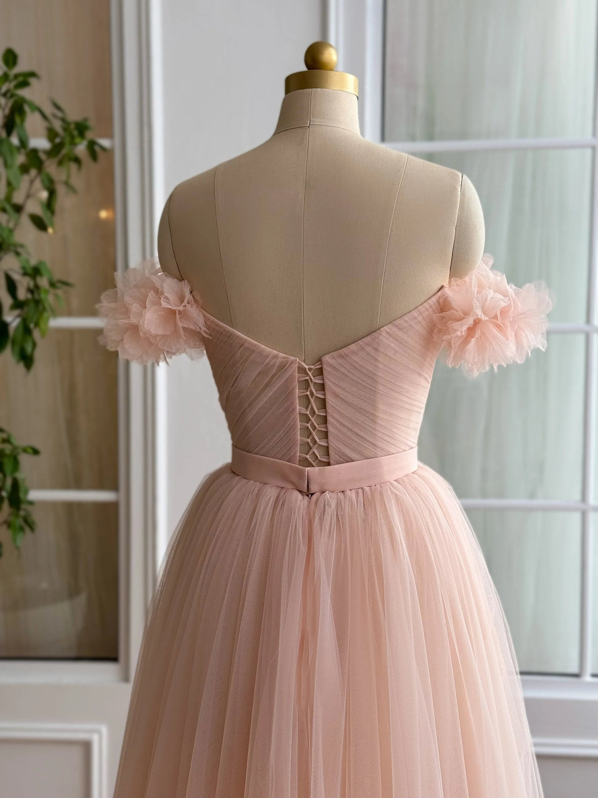Peach off-shoulder prom dress on mannequin, ruffle sleeves and pleated A-line skirt
