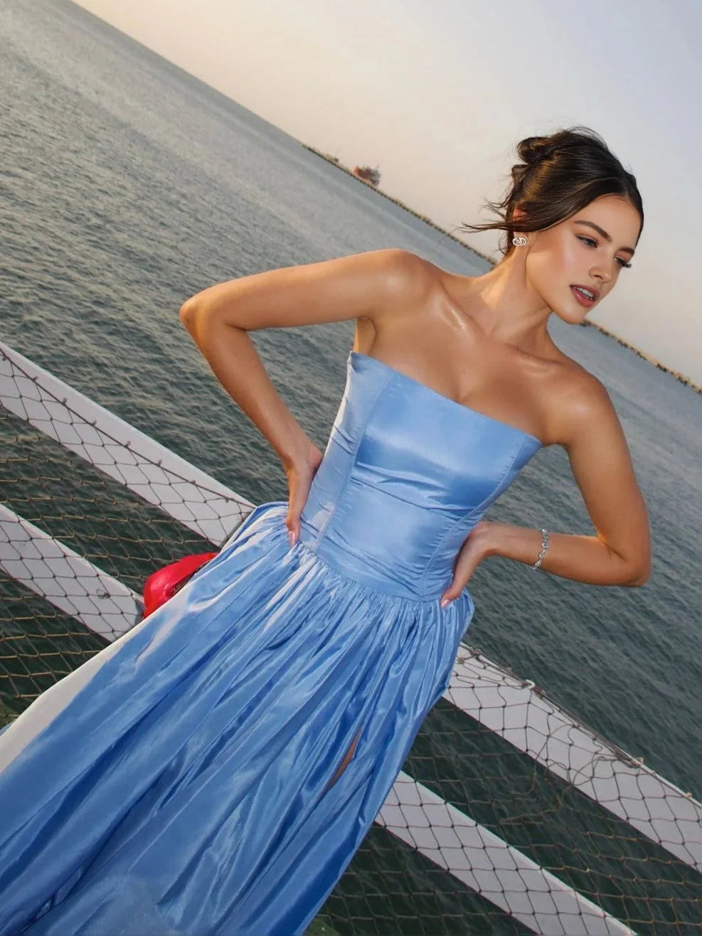 Blue strapless satin ball gown with tiered ruffles and side slit, red rosette detail