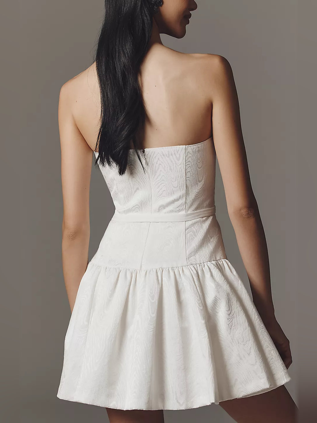 Back view of white strapless mini dress with ruched waist and flared tiered skirt