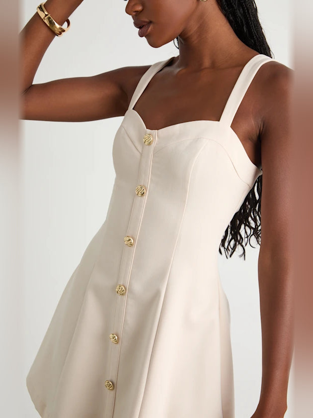 Cream mini dress close-up showing gold button placket and square neckline straps