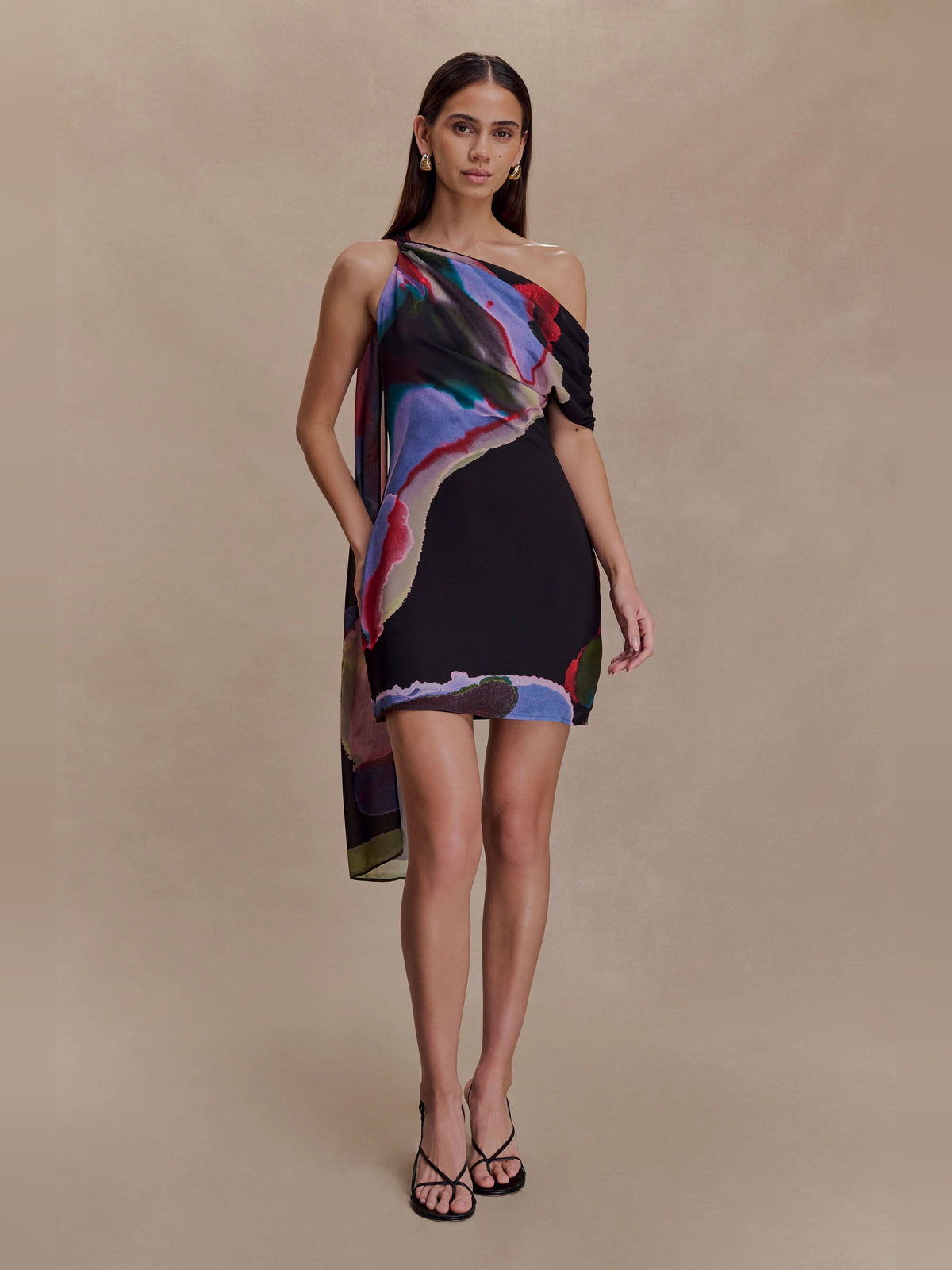 Black one-shoulder mini dress with multicolor abstract print and draped neckline detail.