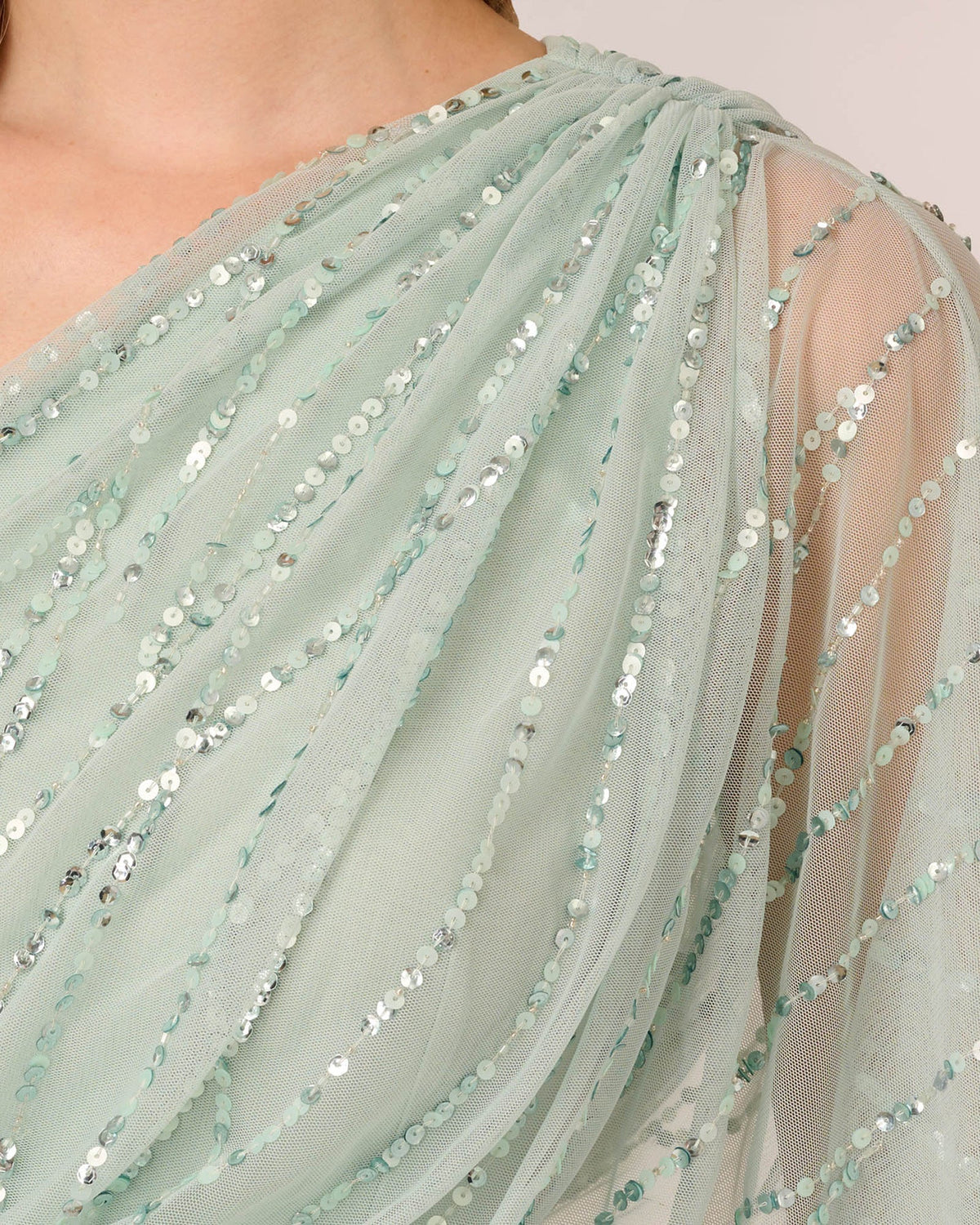 Close-up of mint green one-shoulder draped mesh with silver sequin strands and beads