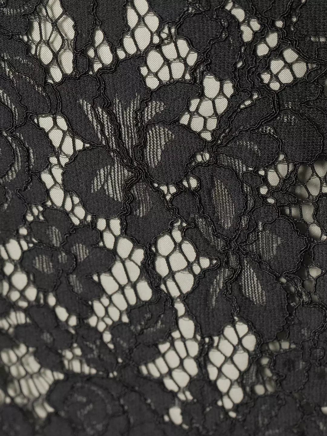 Close-up of black lace overlay with floral-inspired pattern and scalloped edges