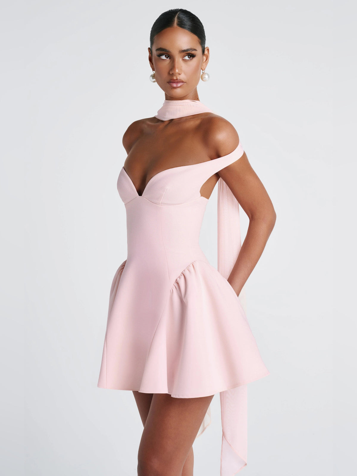 Blush mini dress on mannequin: sweetheart neckline, off-shoulder bodice, gathered waist, long sash back.