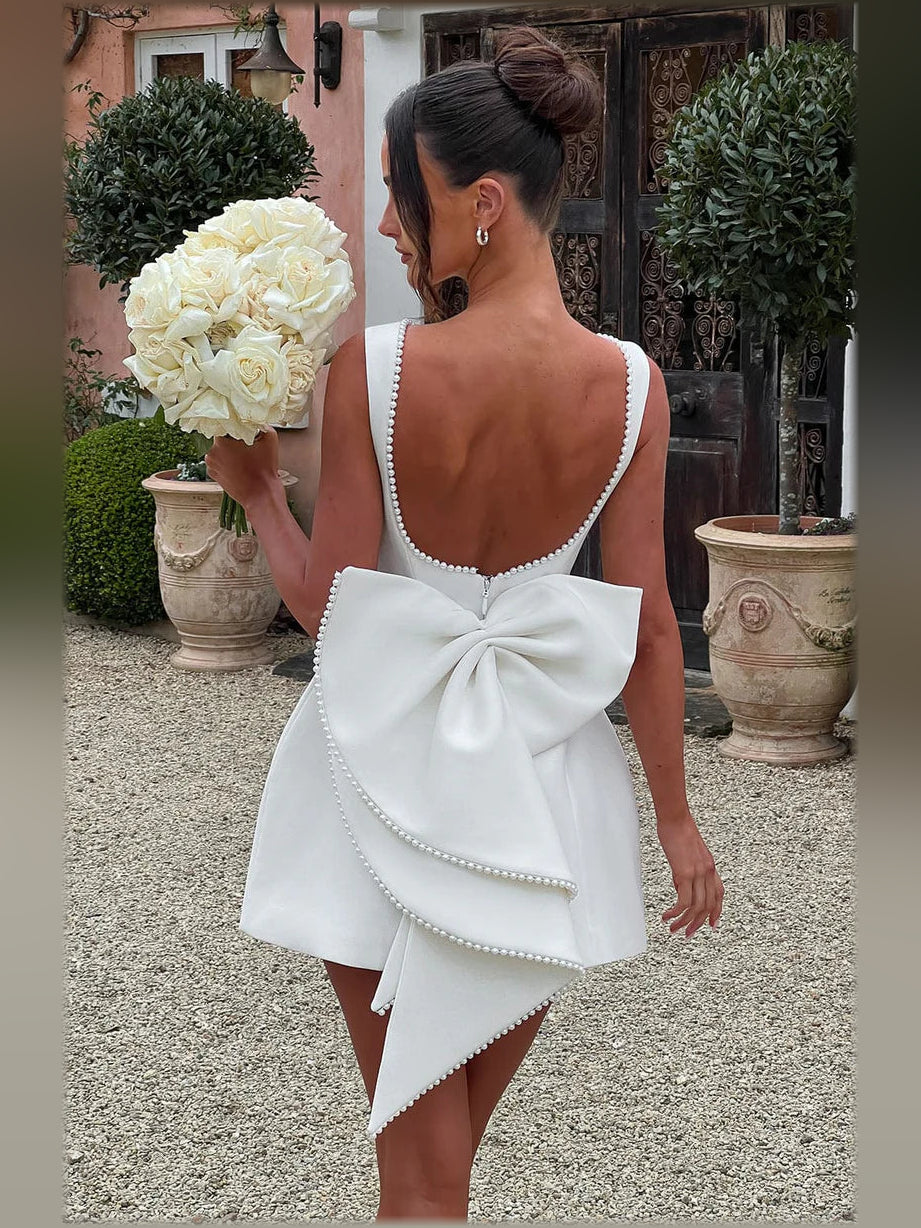 White open-back mini dress with pearl trim and large bow drape at back