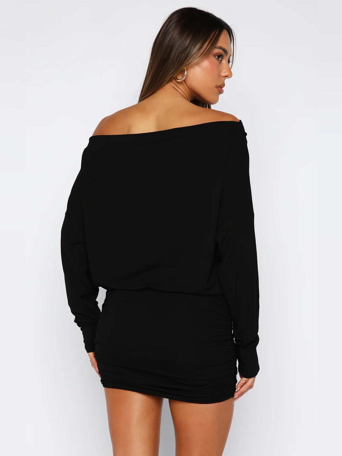 Black long-sleeve mini dress viewed from back, off-shoulder drape and ruched waist.