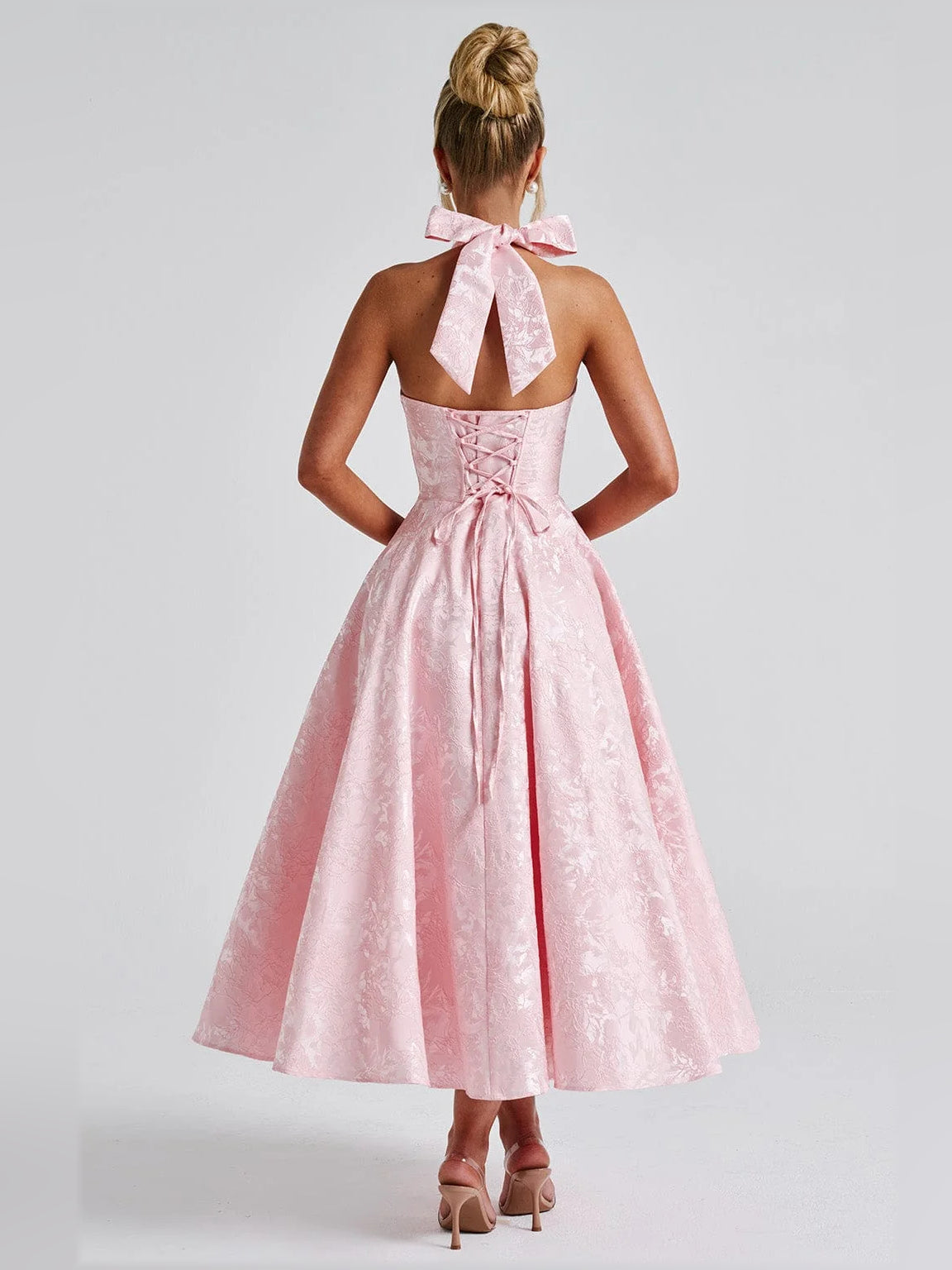 Back view of blush halter midi dress with open back and satin bow, full twirl skirt